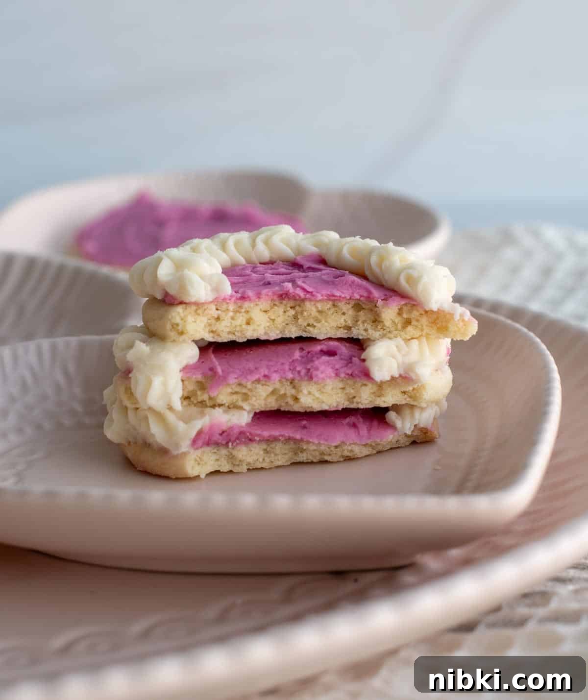 No-Chill Soft Sugar Cookies That Stay Tender and Chewy 15 A stack of three sugar cookies with bites taken out of them sit on a heart shaped white plate.