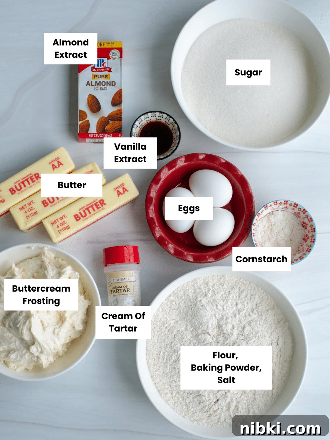 No-Chill Soft Sugar Cookies That Stay Tender and Chewy 4 Ingredients on a counter include sugar, almond extract, vanilla extract, butter, eggs, cornstarch, cream of tartar, flour, baking powder, salt, and buttercream frosting.