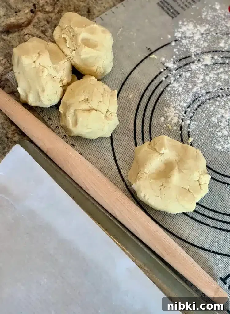 No-Chill Soft Sugar Cookies That Stay Tender and Chewy 6 Balls of cookie dough sit on a dough mat next to a rolling pin.
