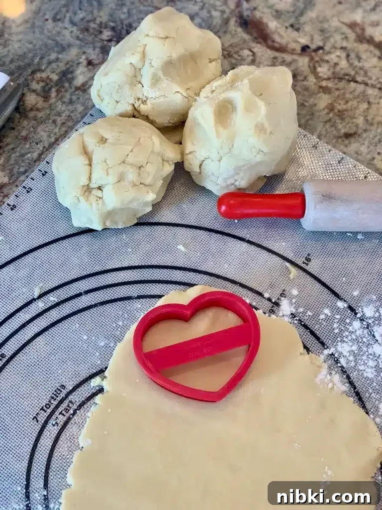 No-Chill Soft Sugar Cookies That Stay Tender and Chewy 8 Dough is rolled out on a pastry mat and a heart shaped cookie cutter is poised over the rolled out dough.