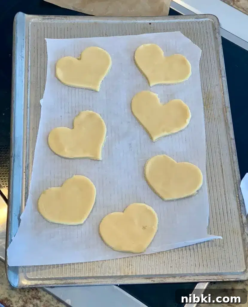 No-Chill Soft Sugar Cookies That Stay Tender and Chewy 10 Heart shaped cookies are on a parchment lined baking sheet prior to baking.