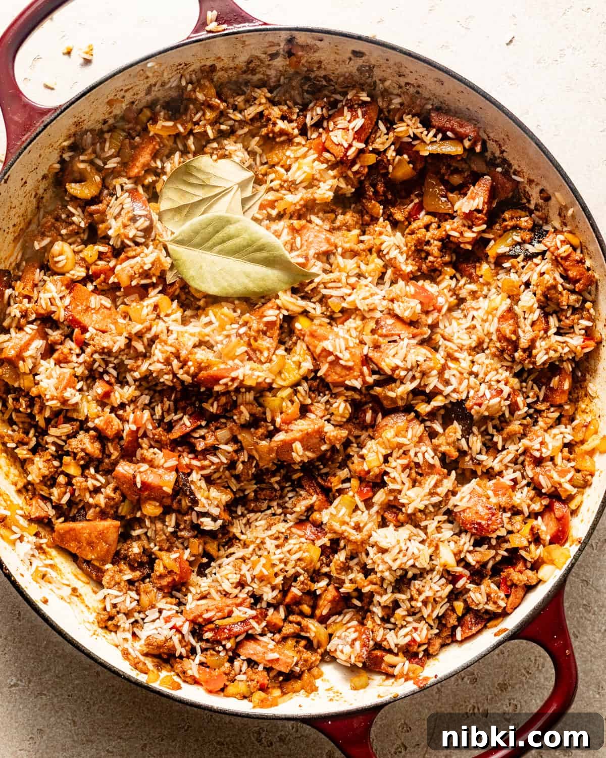 Authentic Louisiana Dirty Rice Recipe 5 dirty rice in a pot with bay leaves, simmering in chicken broth.