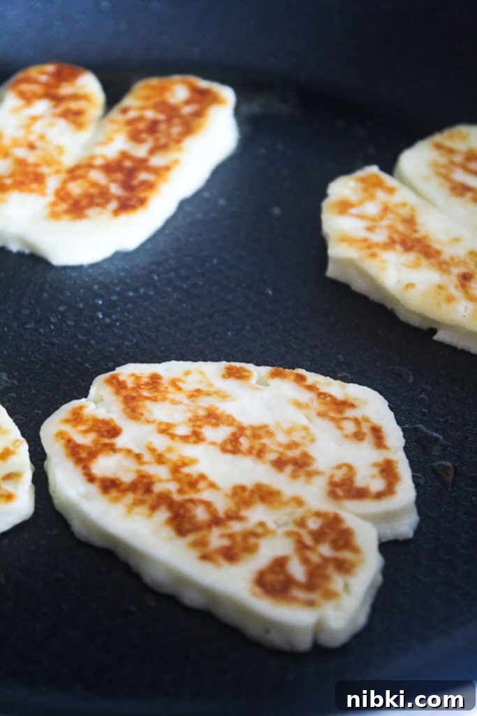 Crispy Grilled or Pan-Fried Halloumi Recipe 3 Lightly browned fried halloumi slices in a frying pan with olive oil.