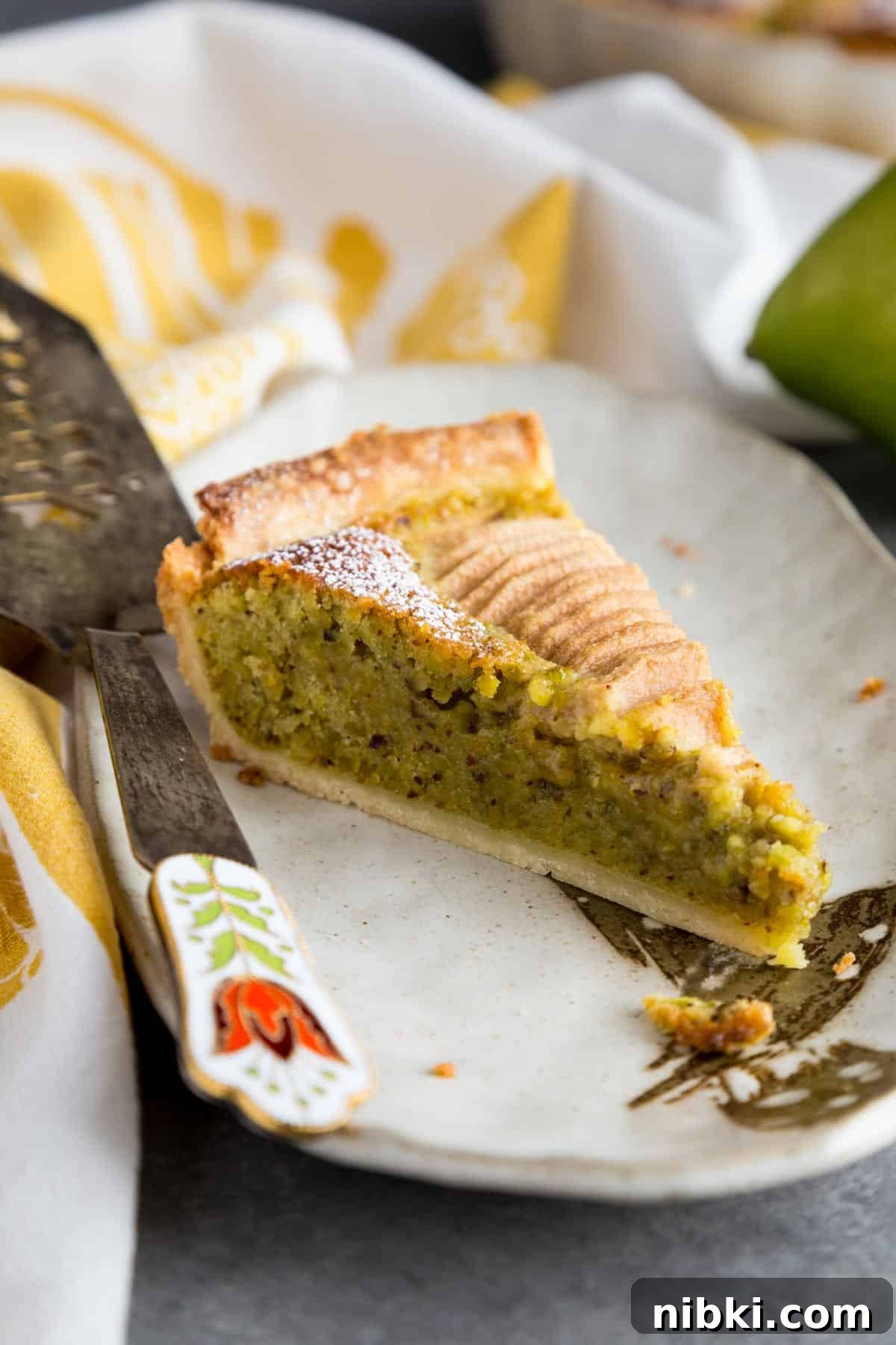 A slice of pear and frangipane tart on a small plate with a decorative pie slicer.
