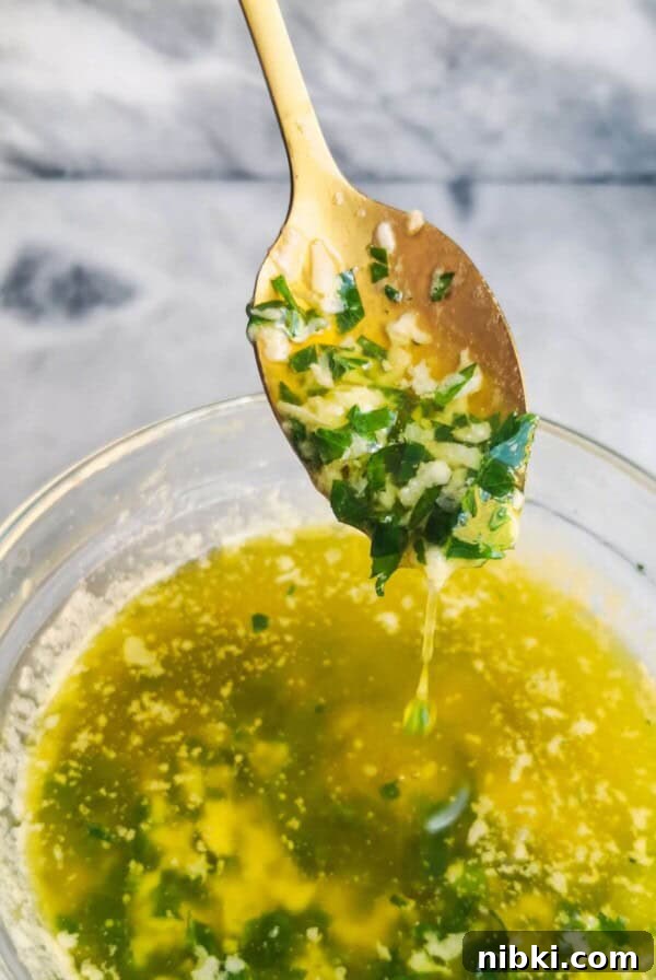 Garlic butter sauce in a small glass bowl, with a gold spoon with sauce on it, on a grey marble background.