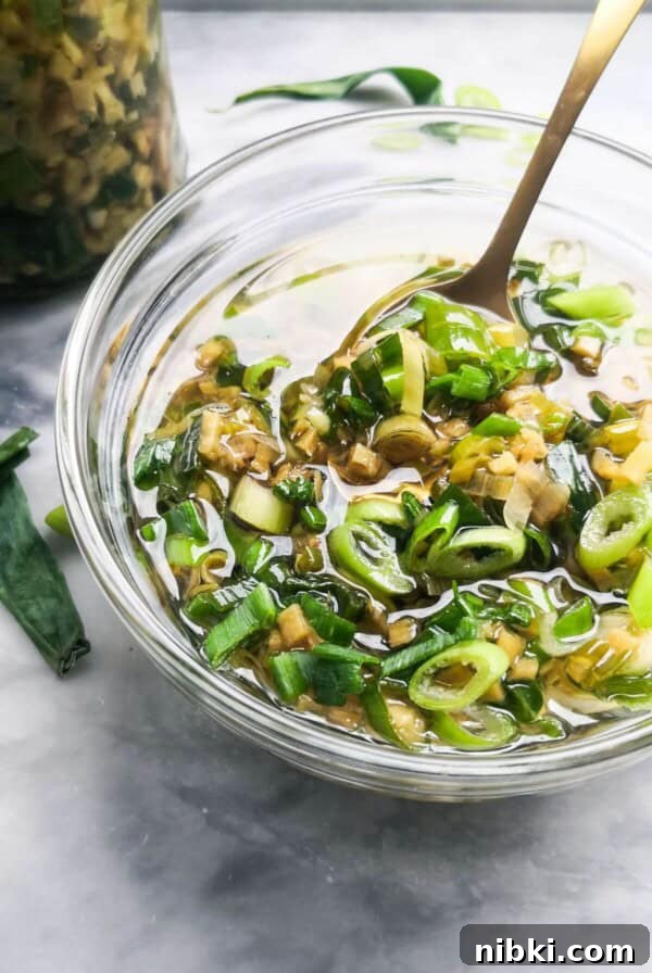 Ginger scallion sauce in a small glass bowl with a gold spoon in it.
