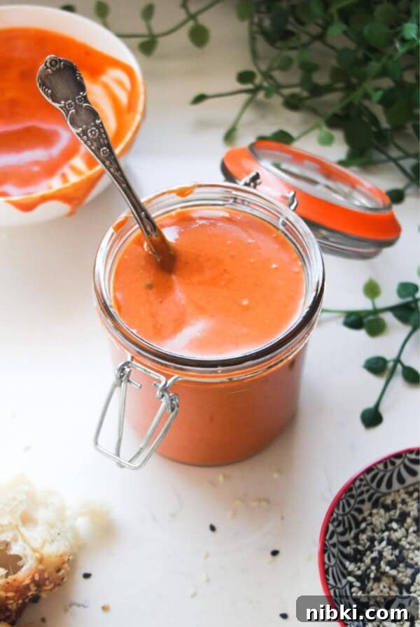 Gochujang mayo in a small glass jar with a bowl of more mayo in the background.