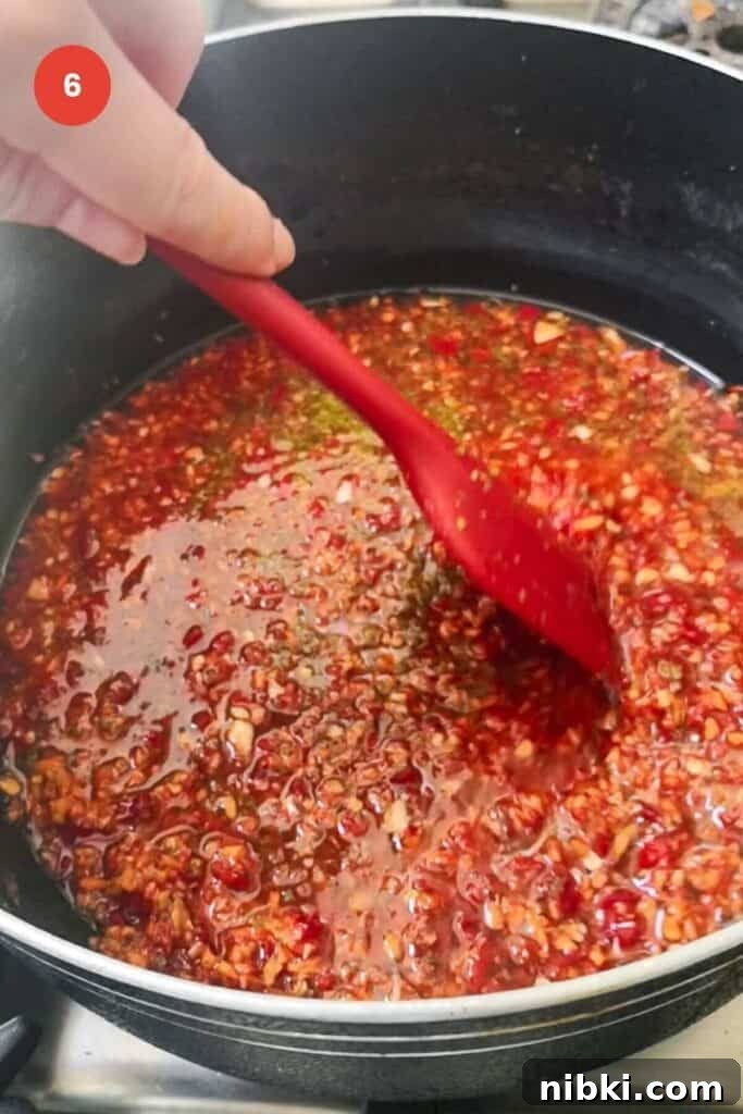 30-Minute Sweet Chili Jam Recipe 8 Red spatula stirring chili jam in a large pot.