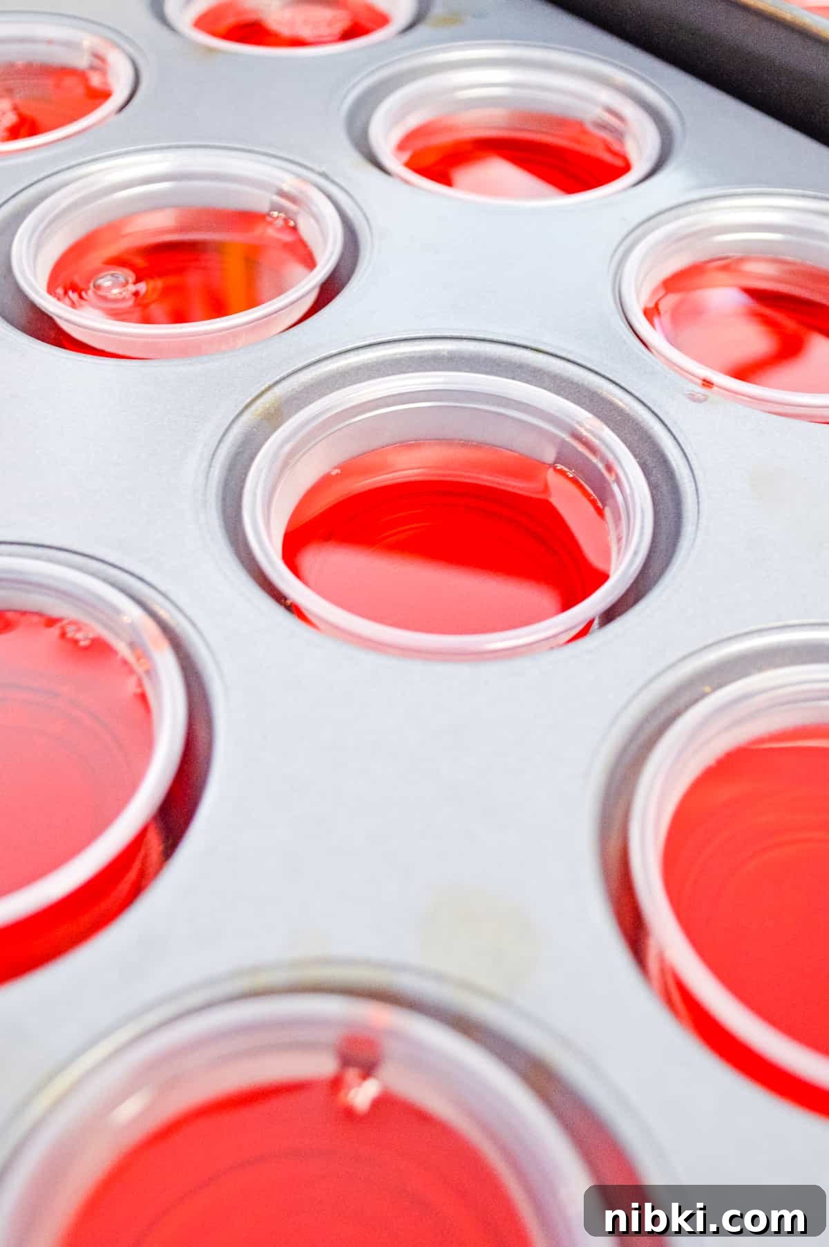 How to Make Strawberry Jello Shots for Parties 4 2 ounce plastic cups filled with red liquid in the cavities of a muffin tin