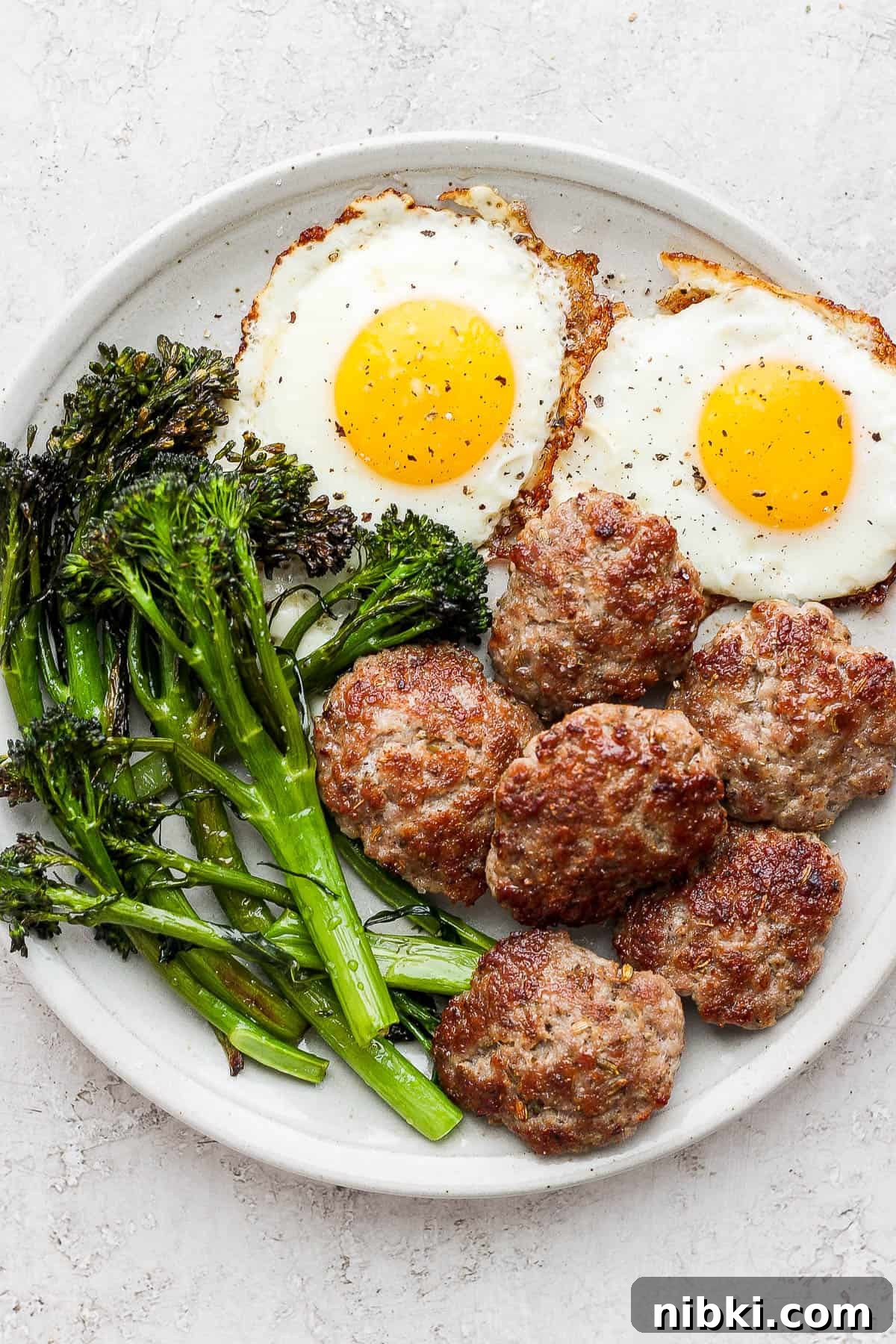 Sausage on a plate with eggs and broccolini.