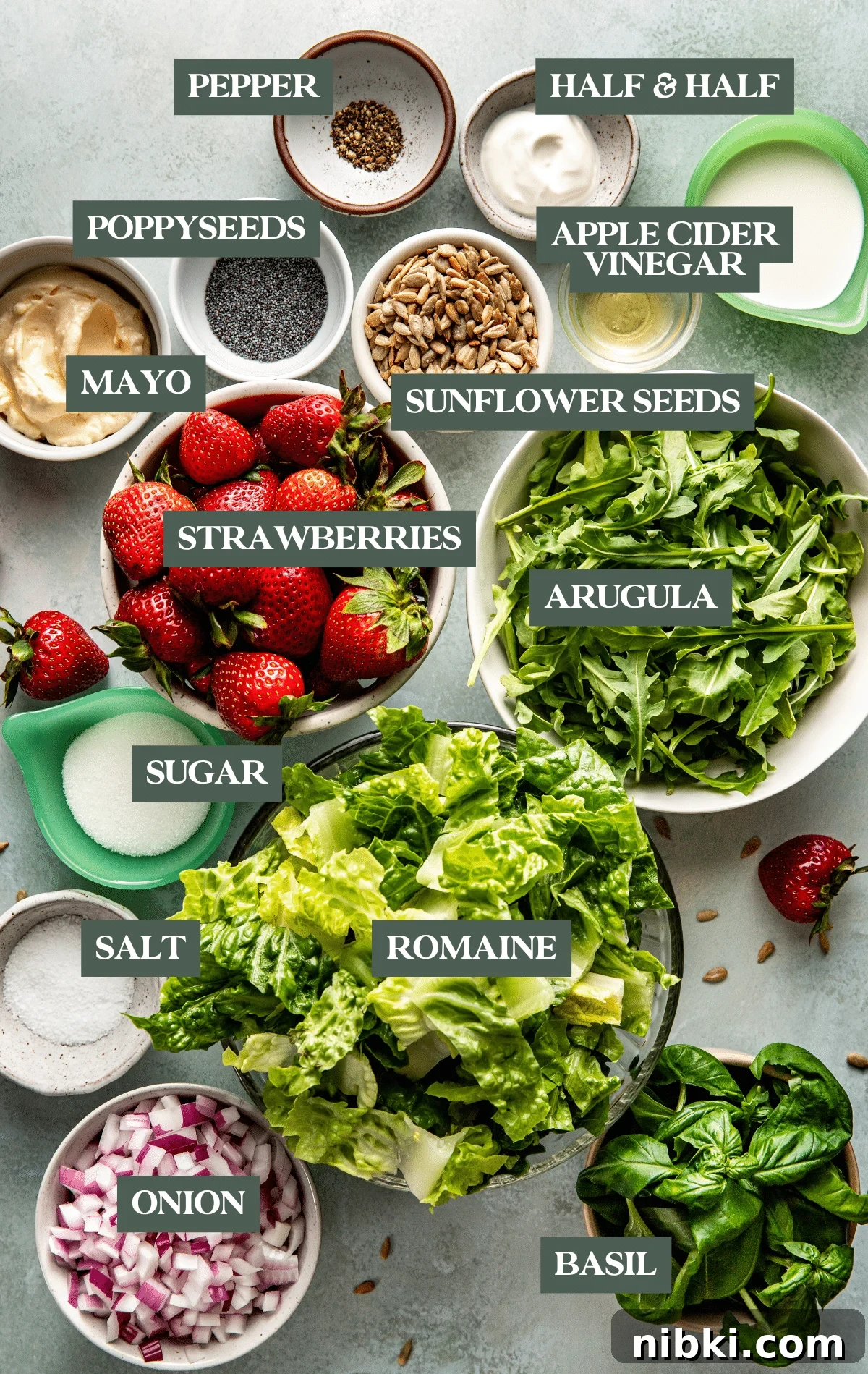 Strawberry Poppyseed Salad with Goat Cheese Croutons 5 Overhead view of fresh salad ingredients laid out before assembly, including strawberries, arugula, romaine, spinach, red onion, sunflower seeds, poppy seeds, mayo, yogurt, milk, vinegar, and sugar.