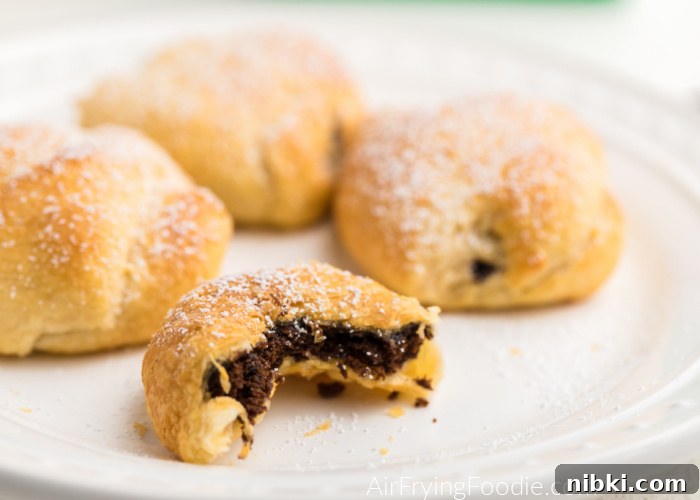 CLose up of fried thin mints on a white plate, sprinkled with powdered sugar - one with a bite missing. 