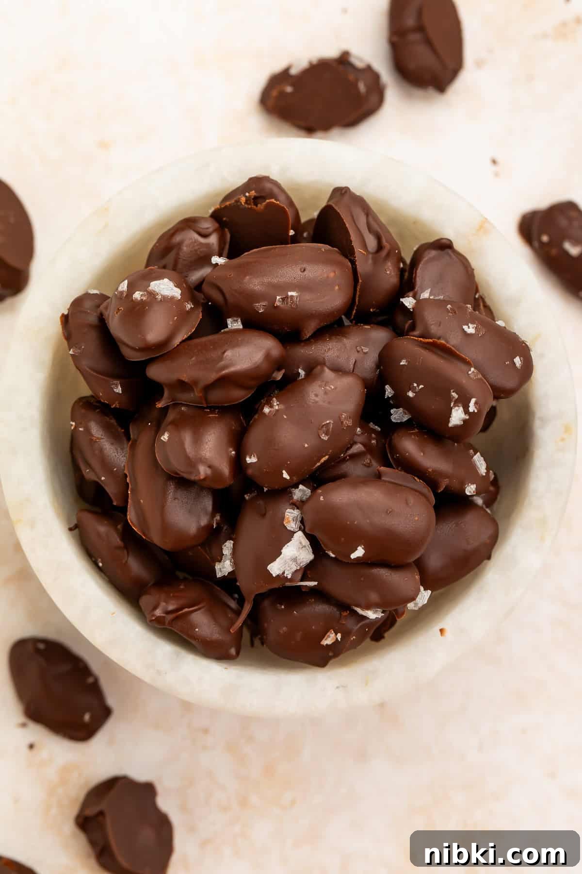 Homemade Chocolate-Covered Almonds Recipe 4 Dark chocolate-covered almonds topped with flaky sea salt in a white bowl.