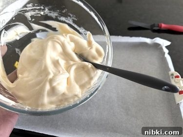 Light coffee-coloured keto Swiss roll mixture being stirred in a bowl beside a lined baking tray.
