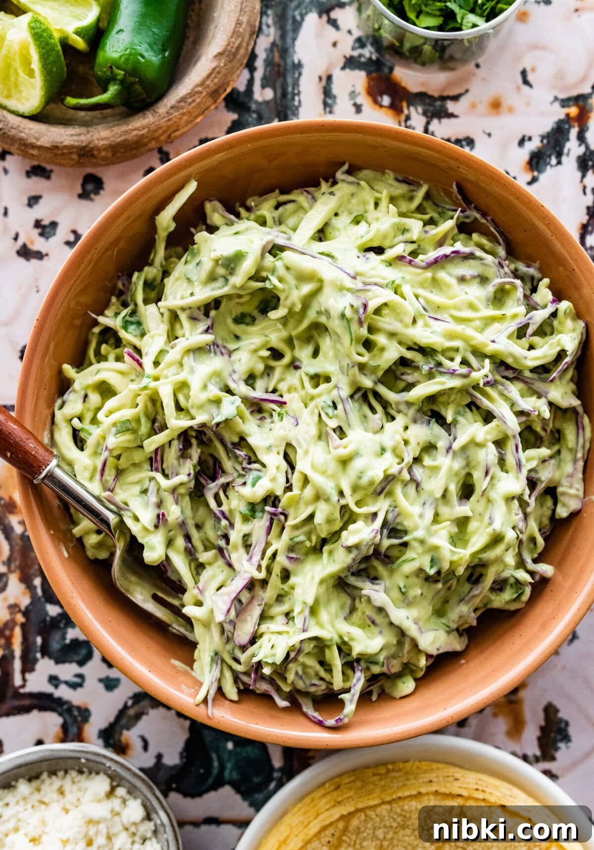 Creamy Avocado Coleslaw Recipe for Summer BBQs 2 creamy avocado slaw in a bowl with a spoon in it.