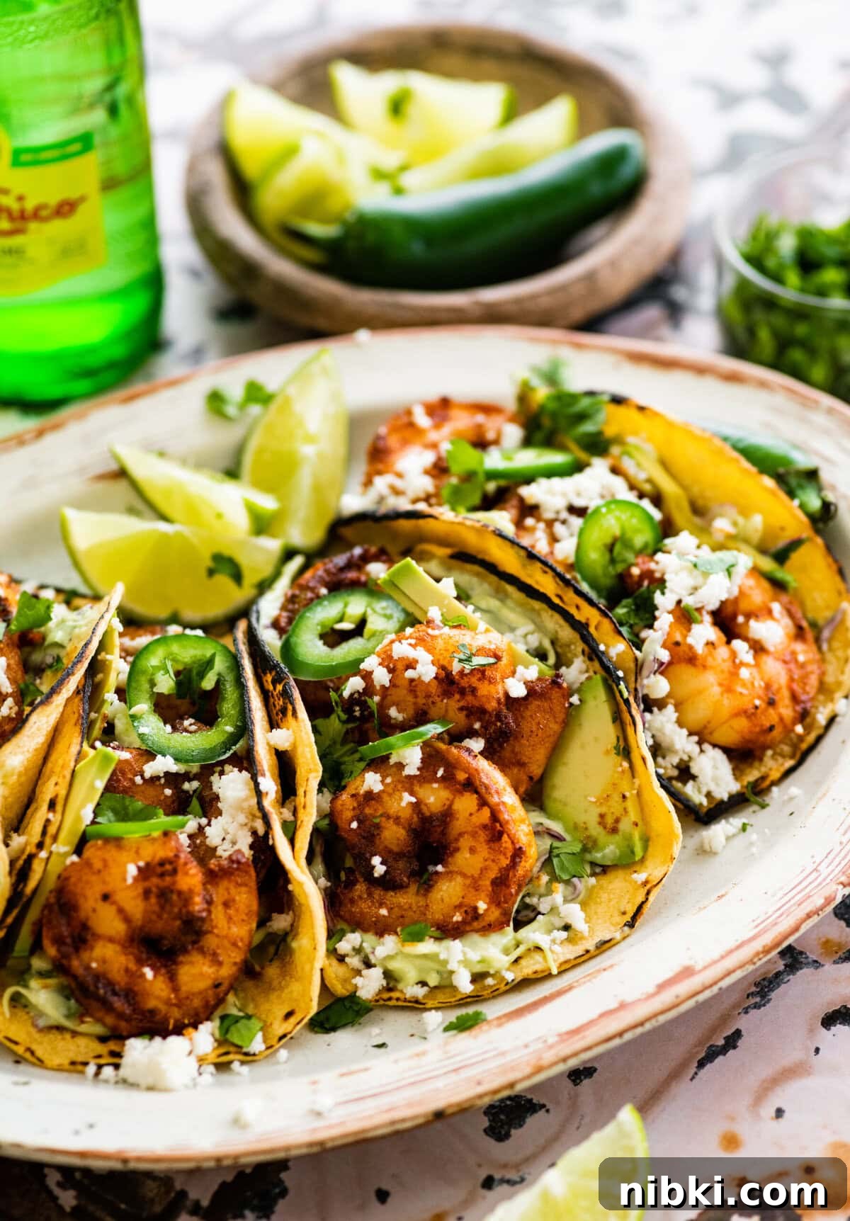 Creamy Avocado Coleslaw Recipe for Summer BBQs 9 assembled shrimp tacos on a serving platter with creamy slaw and all the toppings including limes.