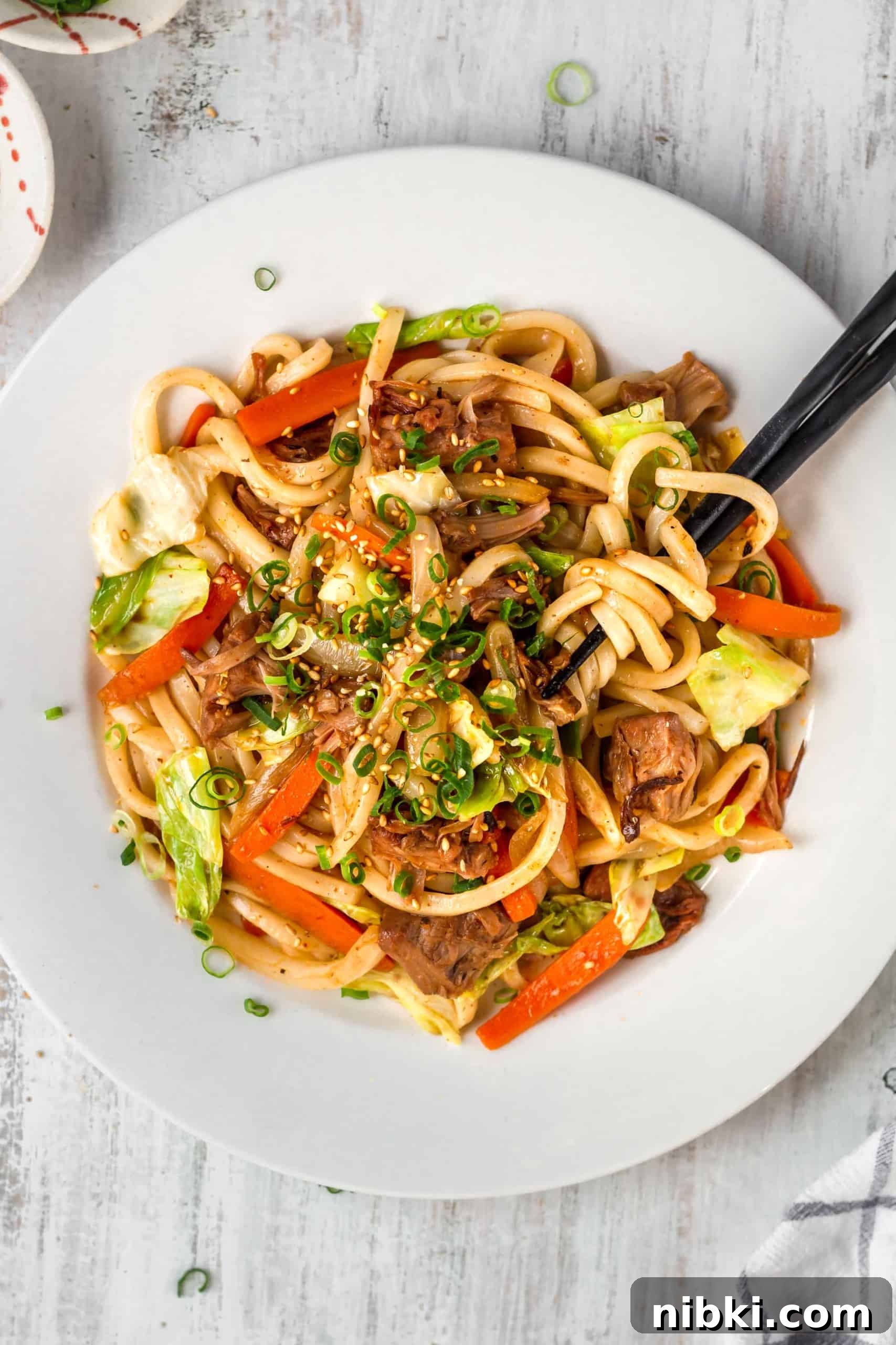 A plate of spicy noodles with black chopsticks