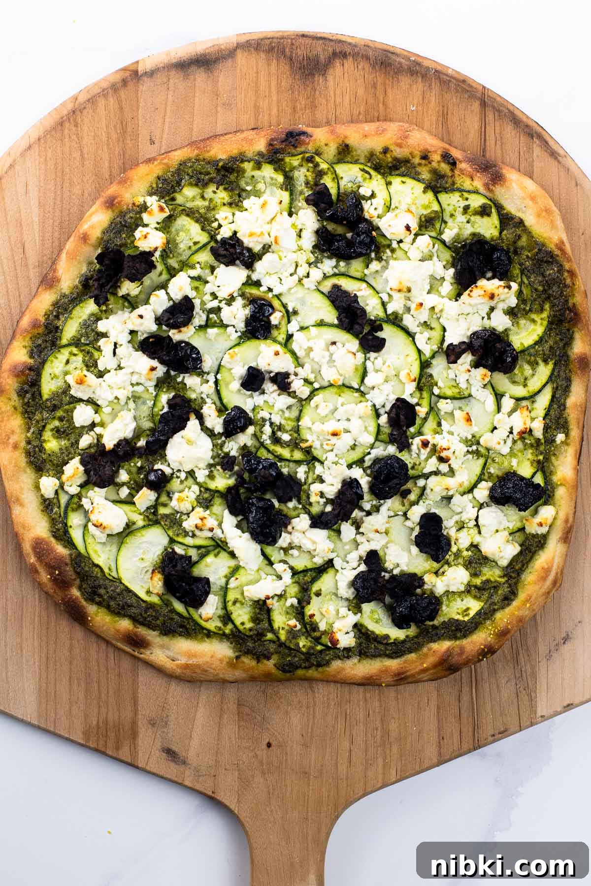 Crispy Pesto and Feta Pizza with Zucchini and Olives 2 pesto and feta pizza with zucchini and black olives on a pizza peel