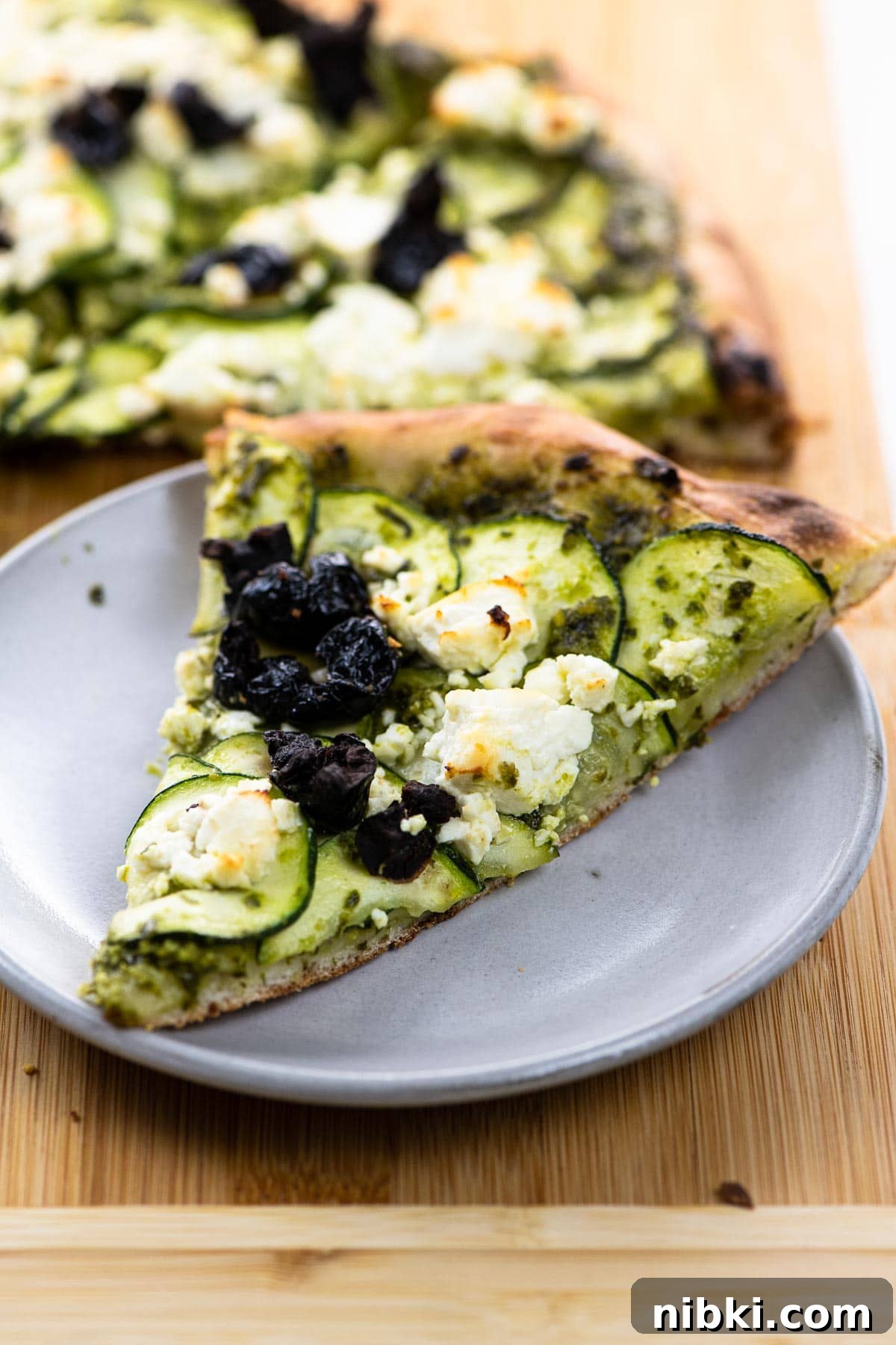 Crispy Pesto and Feta Pizza with Zucchini and Olives 5 pesto and feta pizza with zucchini and black olives on a pizza peel and a plate