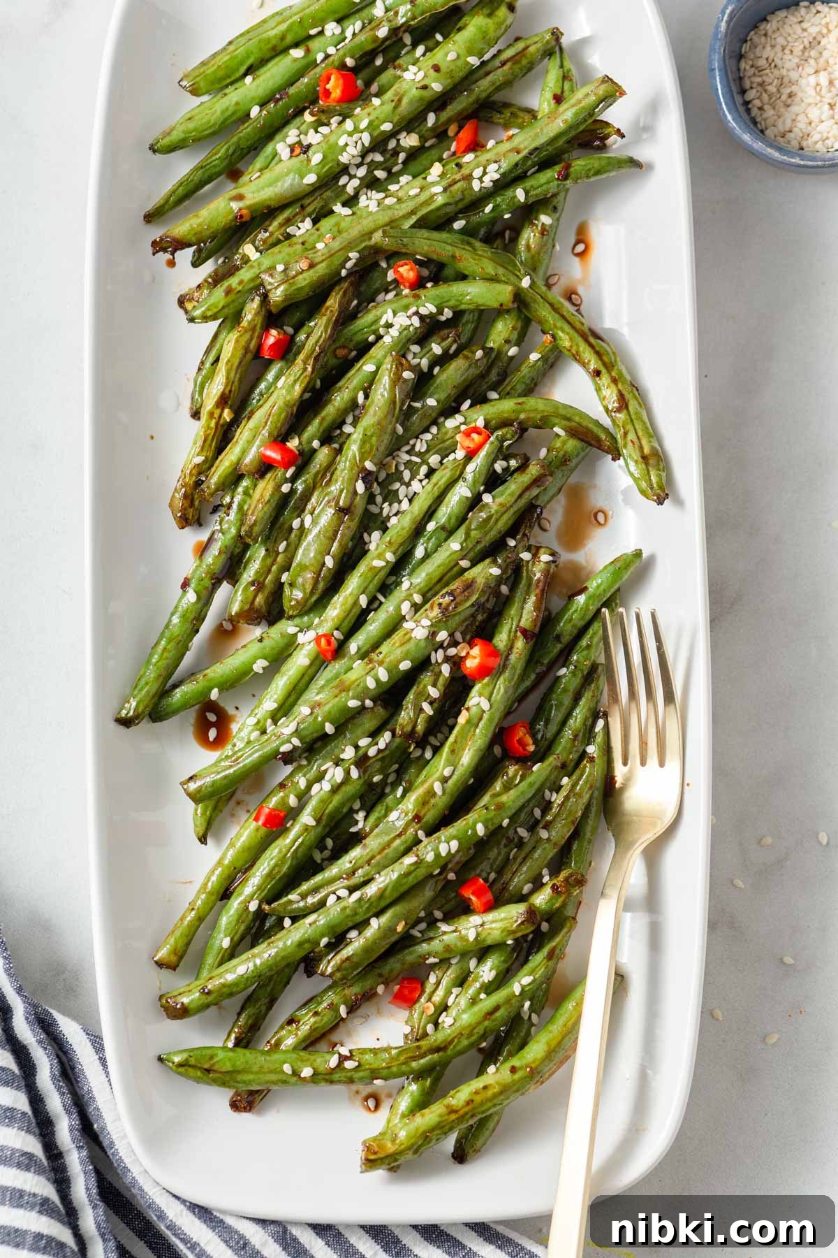 air fryer asian green beans in a plate with a fork and sesame seeds.