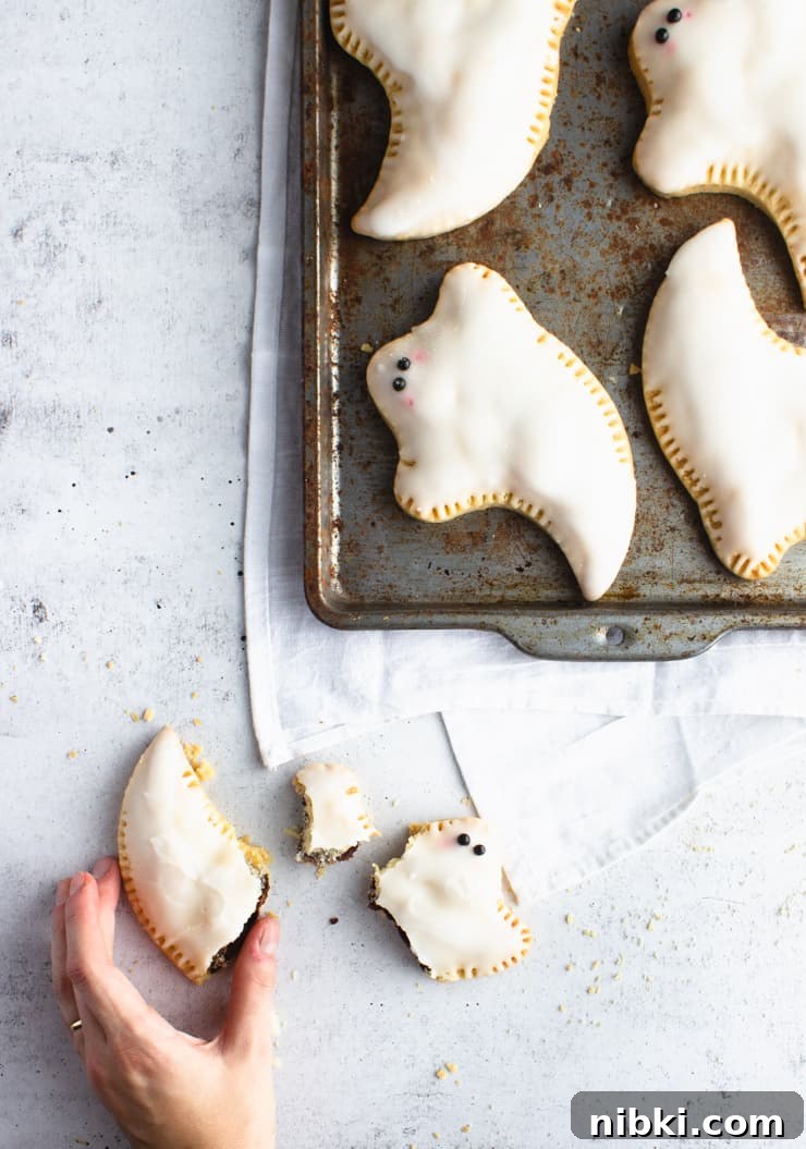 How to Make Pop-Tart Ghosts for Halloween 4 baking sheet with pop tart ghosts and one broken ghost outside the sheet with a hand reaching towards it
