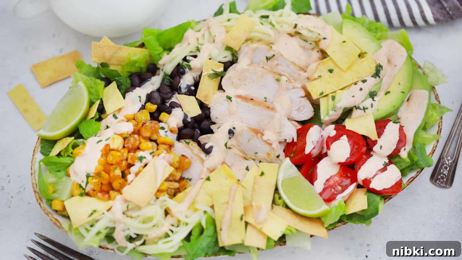 17 Affordable Chicken Recipes That Stretch Your Grocery Budget 13 A colorful chicken salad with avocado, black beans, corn, cherry tomatoes, and lime slices, presented in a white bowl.