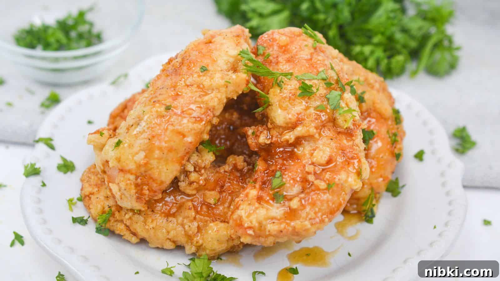 17 Affordable Chicken Recipes That Stretch Your Grocery Budget 8 Fried chicken with honey glaze garnished with parsley on a white plate.