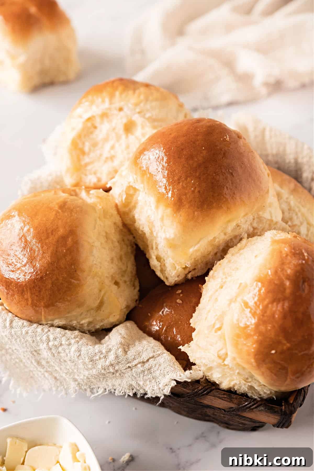 Soft Homemade Yeasted Dinner Rolls 2 Several dinner rolls in a basket with beige cloth. White background.