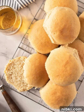 A pile of beer dinner rolls on a wire rack. Glass of beer, white marbled surface.