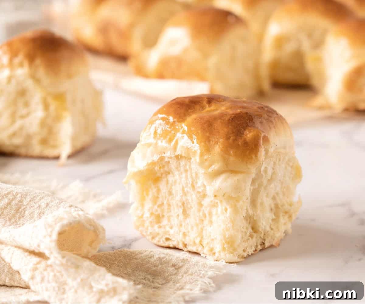 Soft Homemade Yeasted Dinner Rolls 5 Soft dinner roll on a white marbled surface. More rolls in the background.