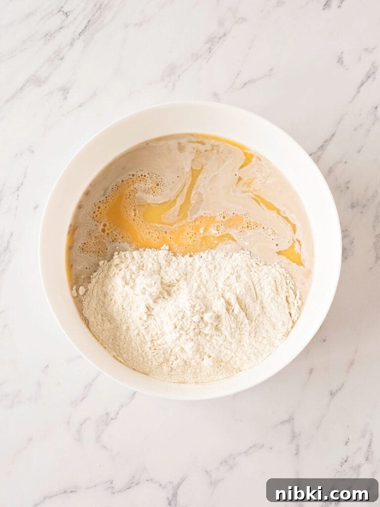 Soft Homemade Yeasted Dinner Rolls 6 Flour and wet ingredients for bread in a white bowl. Top view. White marbled surface.