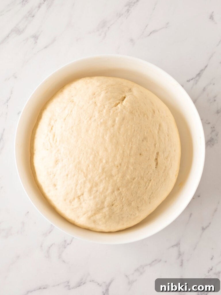 Soft Homemade Yeasted Dinner Rolls 9 Doubled bread dough in a white bowl. Top view. White marbled surface.