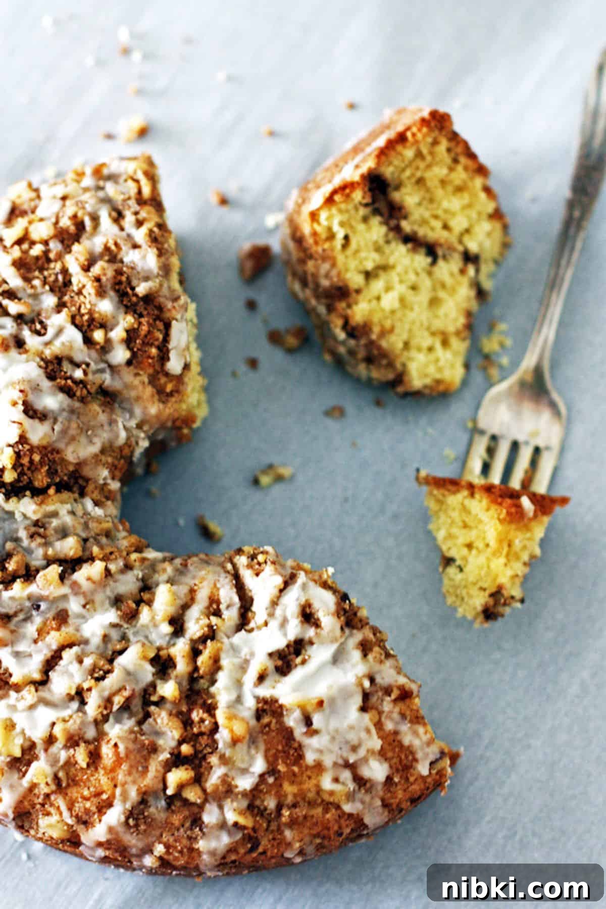 Moist Cinnamon Streusel Coffee Cake Recipe 7 Half of a glazed coffee cake with a bite on a fork and a slice showing a cinnamon layer in the middle.