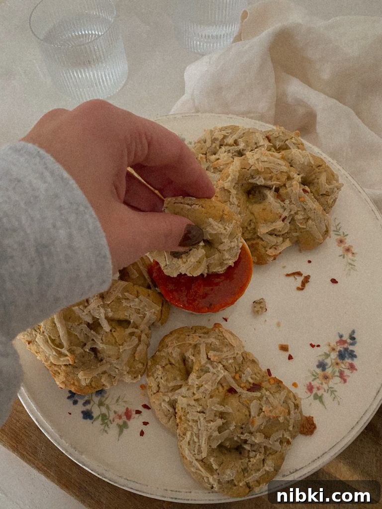 Gluten-Free Dairy-Free Soft Pizza Pretzels Without Yeast 2 soft pizza pretzels on a white floral plate with hand dipping pretzel in a small bowl of marinara