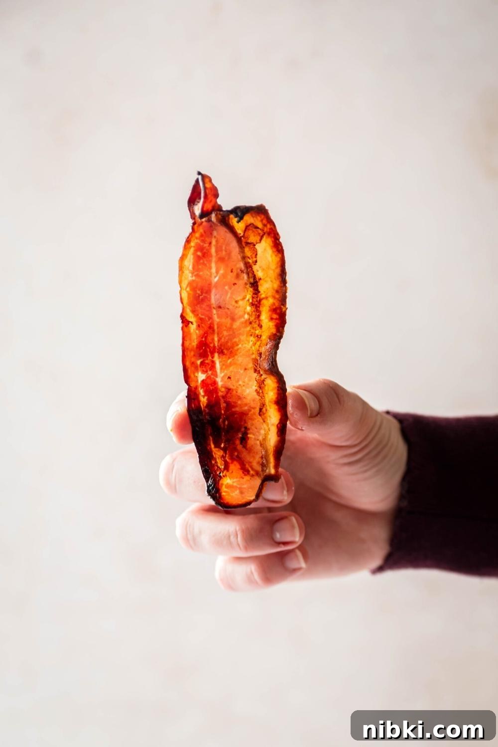 A hand holding a slice of turkey bacon vertically.