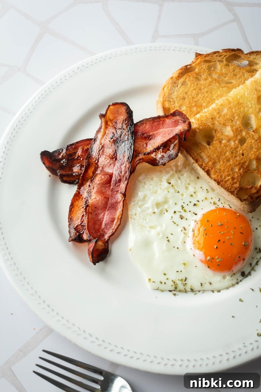 Part of a white plate with two slices of turkey bacon, an egg, and toast.