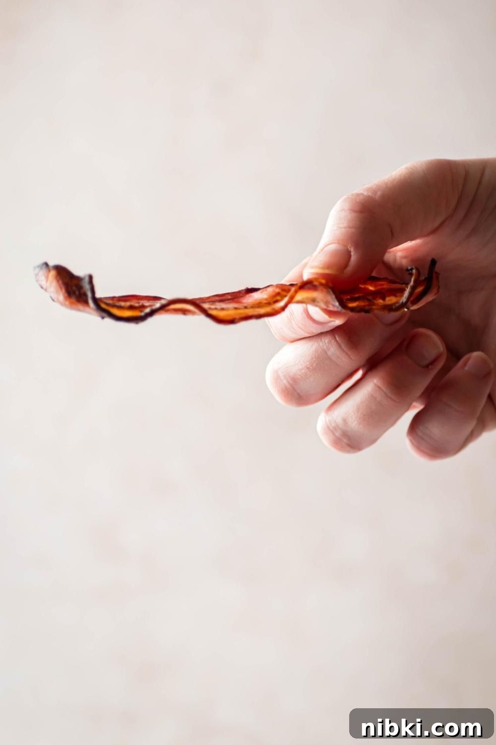 A hand holding a slice of turkey bacon horizontally.
