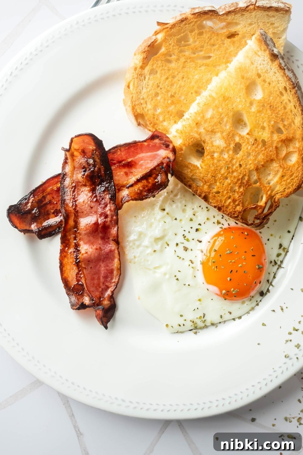 Two slices of turkey bacon, an egg, and toast on a white plate.