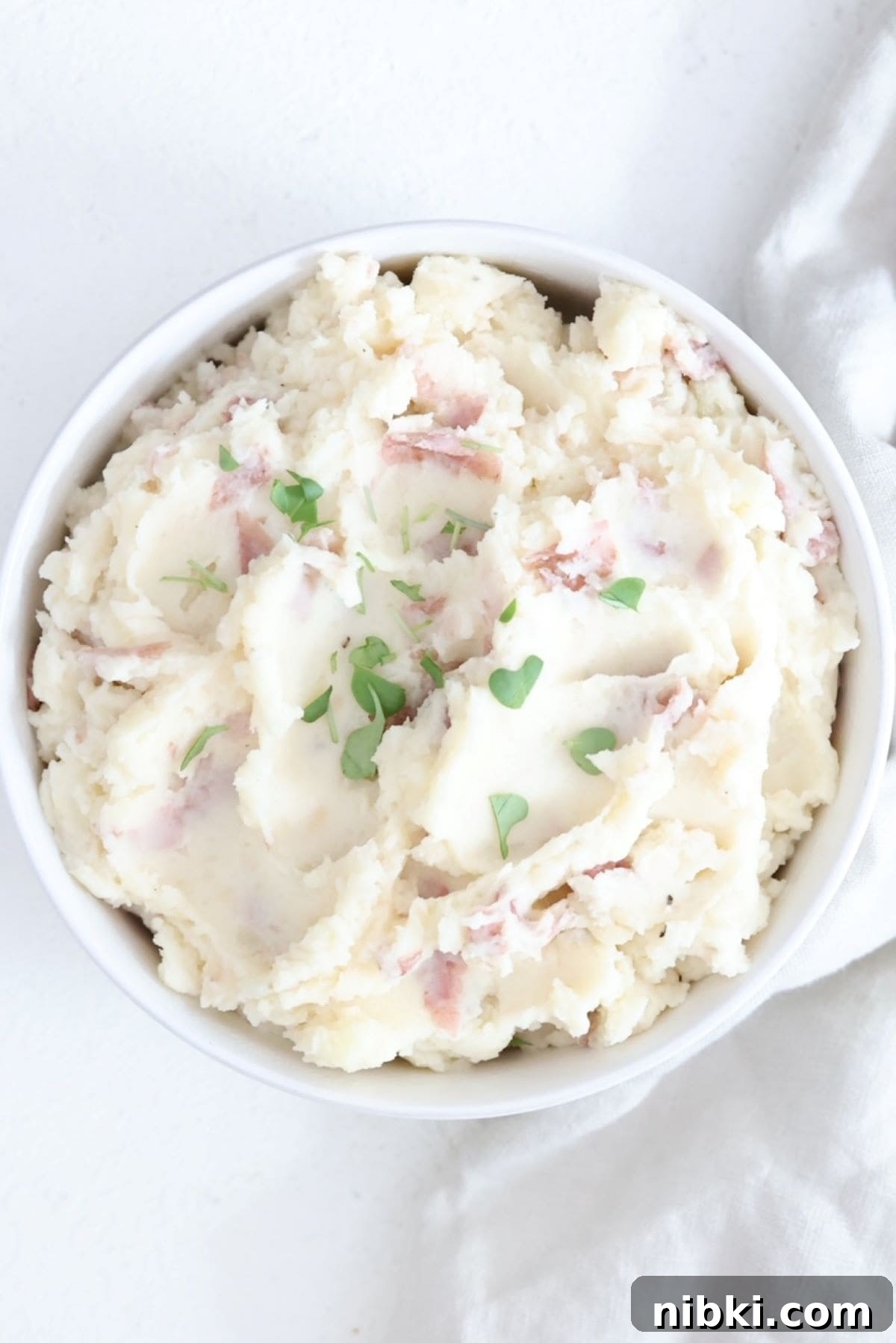 Creamy Mashed Red-Skinned Potatoes 2 A white bowl filled with red skinned mashed potatoes topped with a few microgreens.