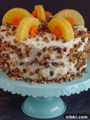 whole carrot cake decorated with pineapple and carrots on a aqua cake stand