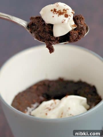 chocolate mug cake being held up on a spoon over cake in a mug