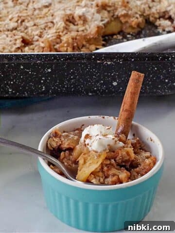 ww apple crisp in a small blue dish with green apple and pan of more apple crisp in the background