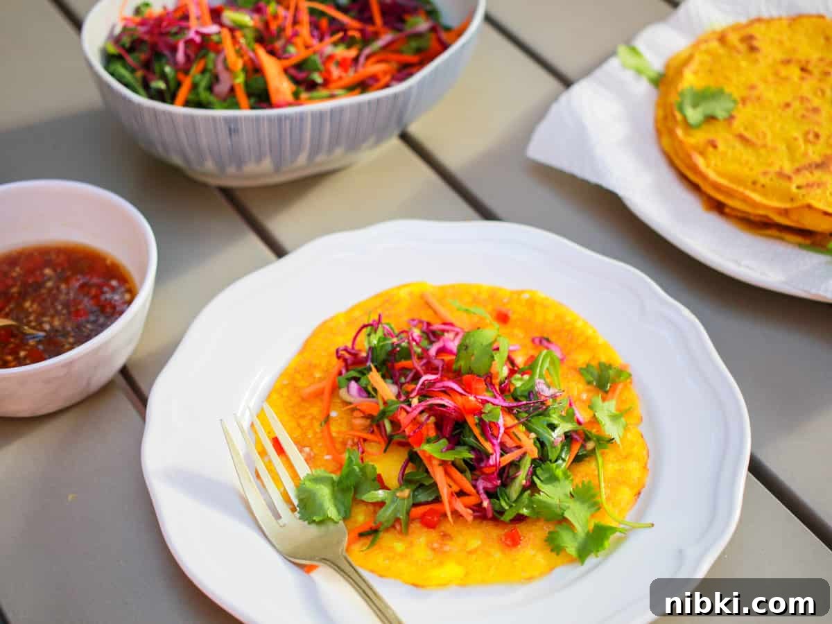 How to Make Crispy Vietnamese Bánh Xèo 2 Photo of a plate with an open pancake with a pile of colourful salad in the middle all set on a sunny grey table with a pile of pancakes and bowl of salad in the background.