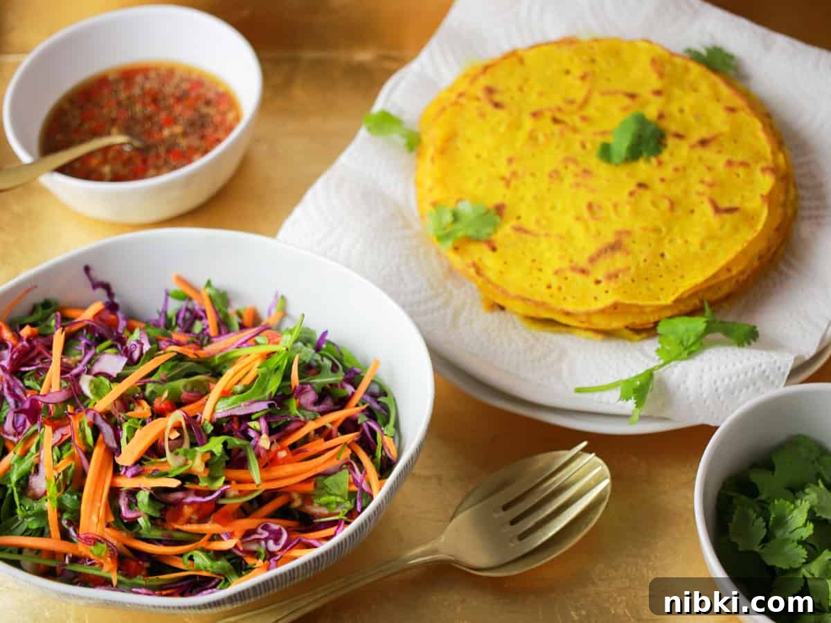How to Make Crispy Vietnamese Bánh Xèo 3 Photo of a tray of the ingredients for the vietnamese banh xeo pancakes with a bowl of salad in the foreground and pancakes piled on a plate in the background plus a bowl of sauce and a bowl of coriander.