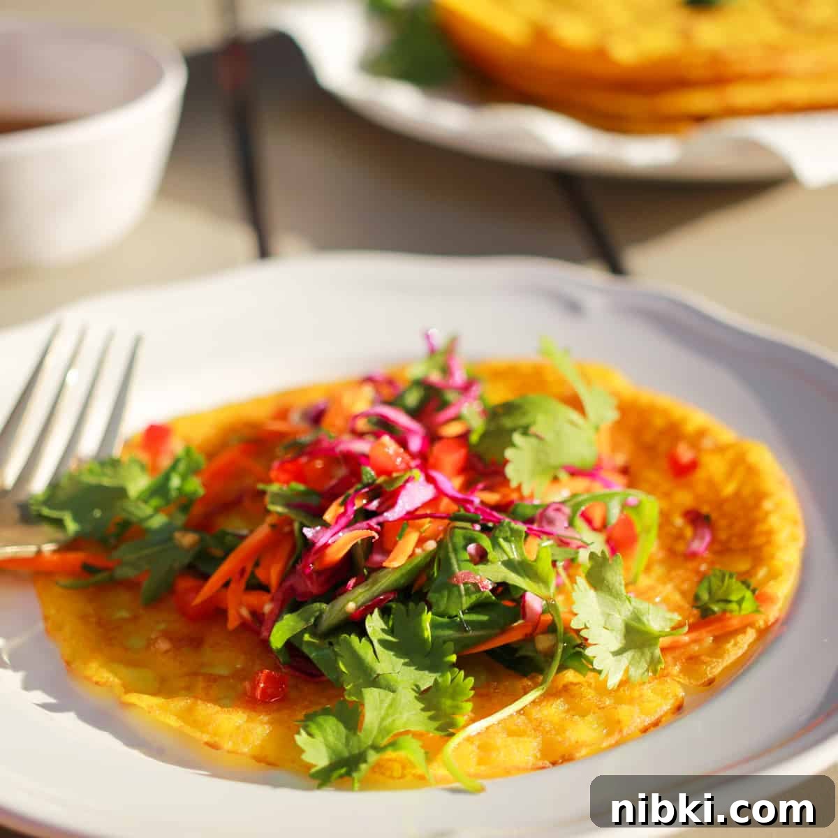 How to Make Crispy Vietnamese Bánh Xèo 4 A close-up photo showing the brightly coloured Vietnamese salad placed on top of an open pancake, on a plate outside in the sunshine.