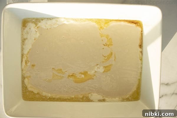 Peach Cobbler Recipe with Golden Biscuit Topping 7 Cobbler batter on the top of melted butter in a white baking dish.