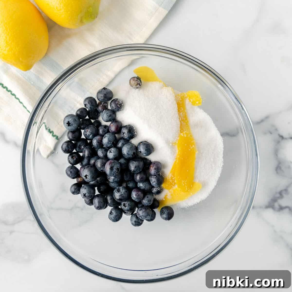 Homemade Blueberry Lemonade Recipe for a Refreshing Summer 2 Blueberries, sugar, and lemon peel in a bowl.