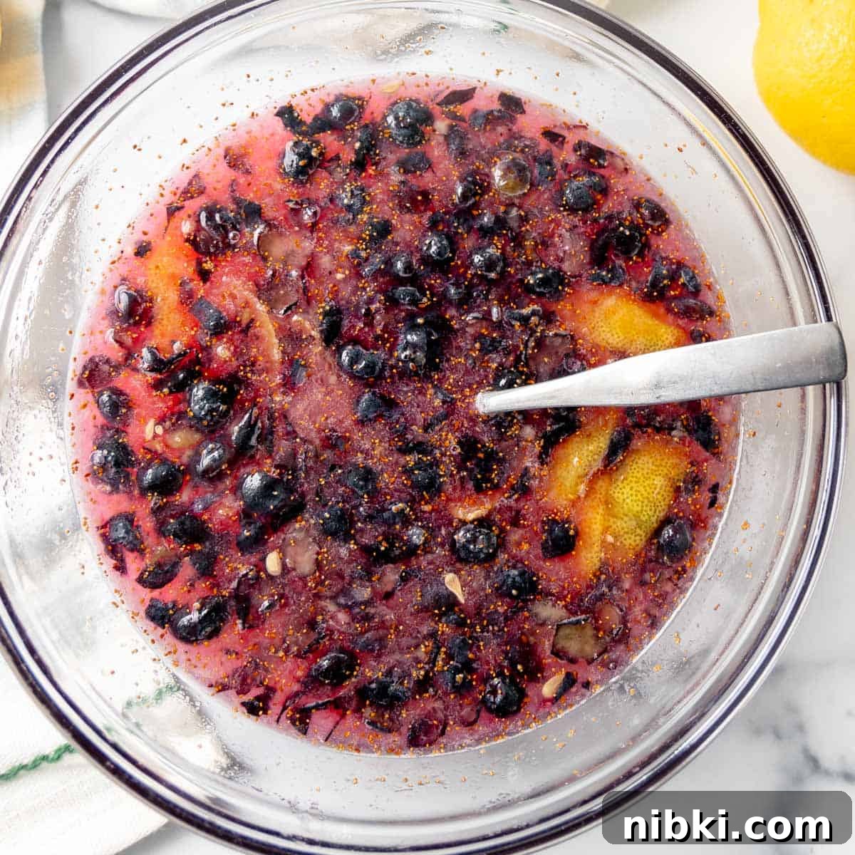 Homemade Blueberry Lemonade Recipe for a Refreshing Summer 5 Blueberries in juice with lemon peel in a glass bowl.