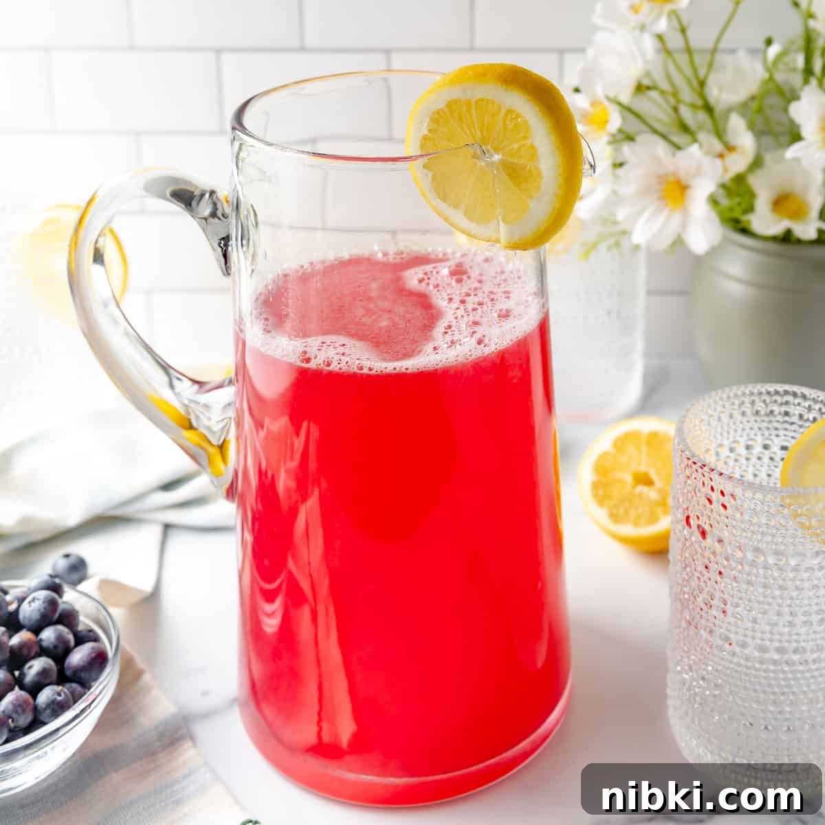 Homemade Blueberry Lemonade Recipe for a Refreshing Summer 7 A pitcher of lemonade with lemon and blueberries on the side.