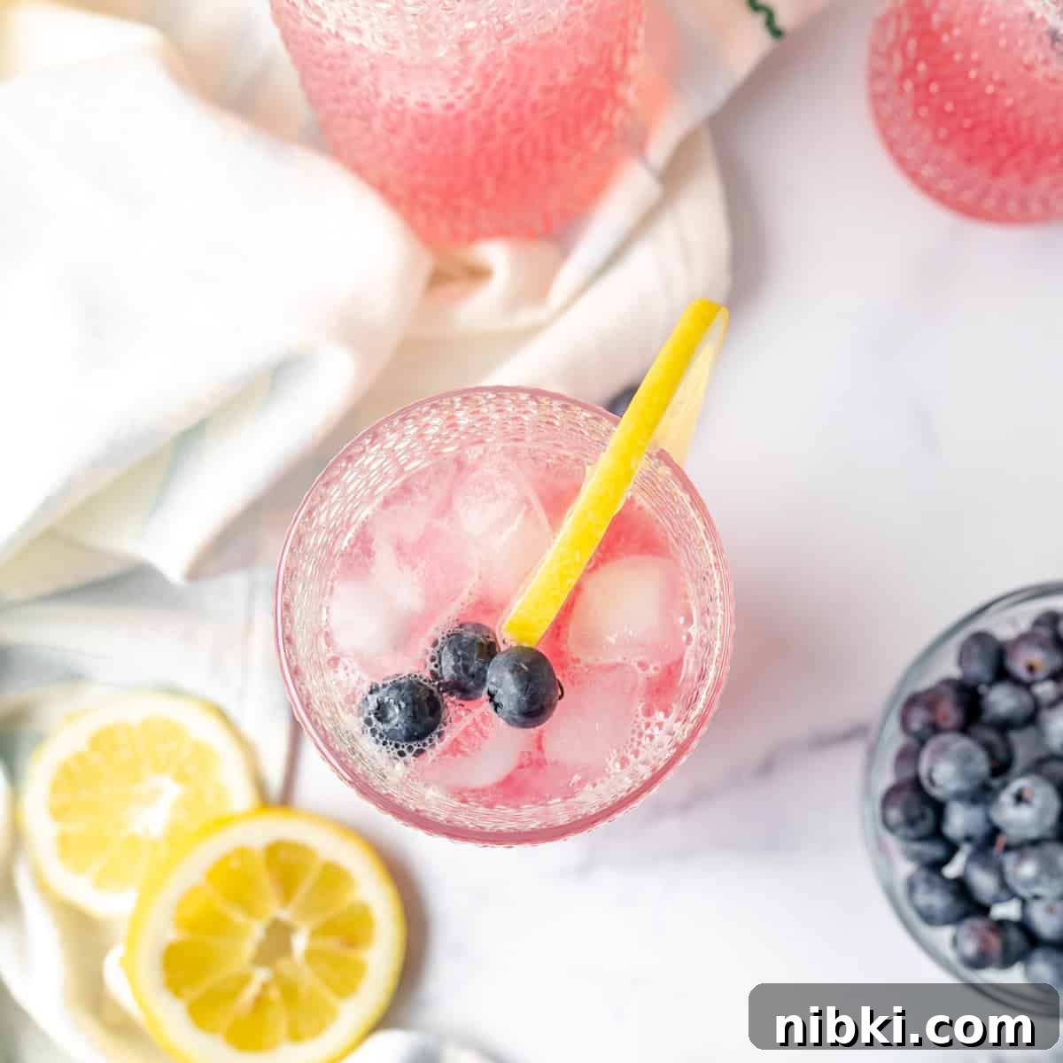Homemade Blueberry Lemonade Recipe for a Refreshing Summer 8 Overhead image of a glass of lemonade with a bowl of blueberries and lemon slices on the side.